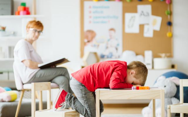 Niño con TDAH mal sentado reclinado sobre una mesa. 